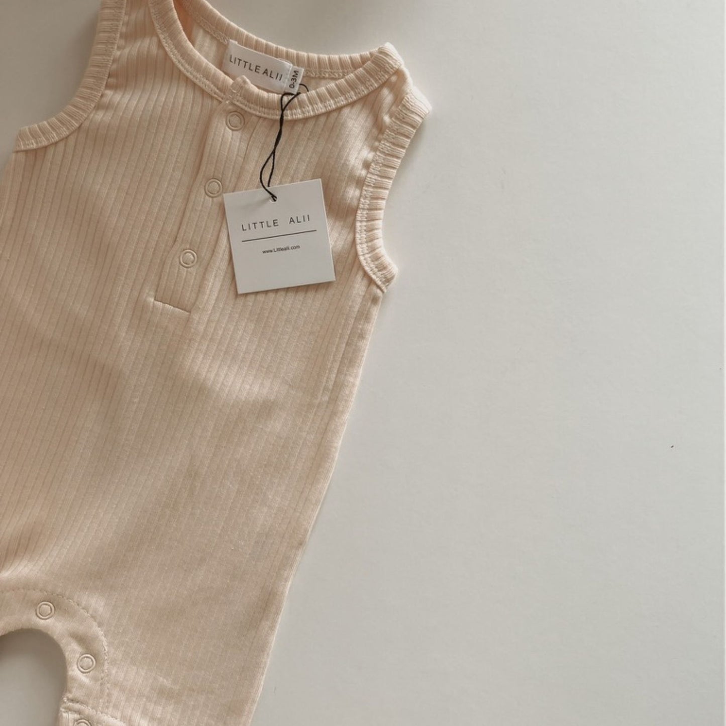 Vanilla baby romper with a tag on a light gray background